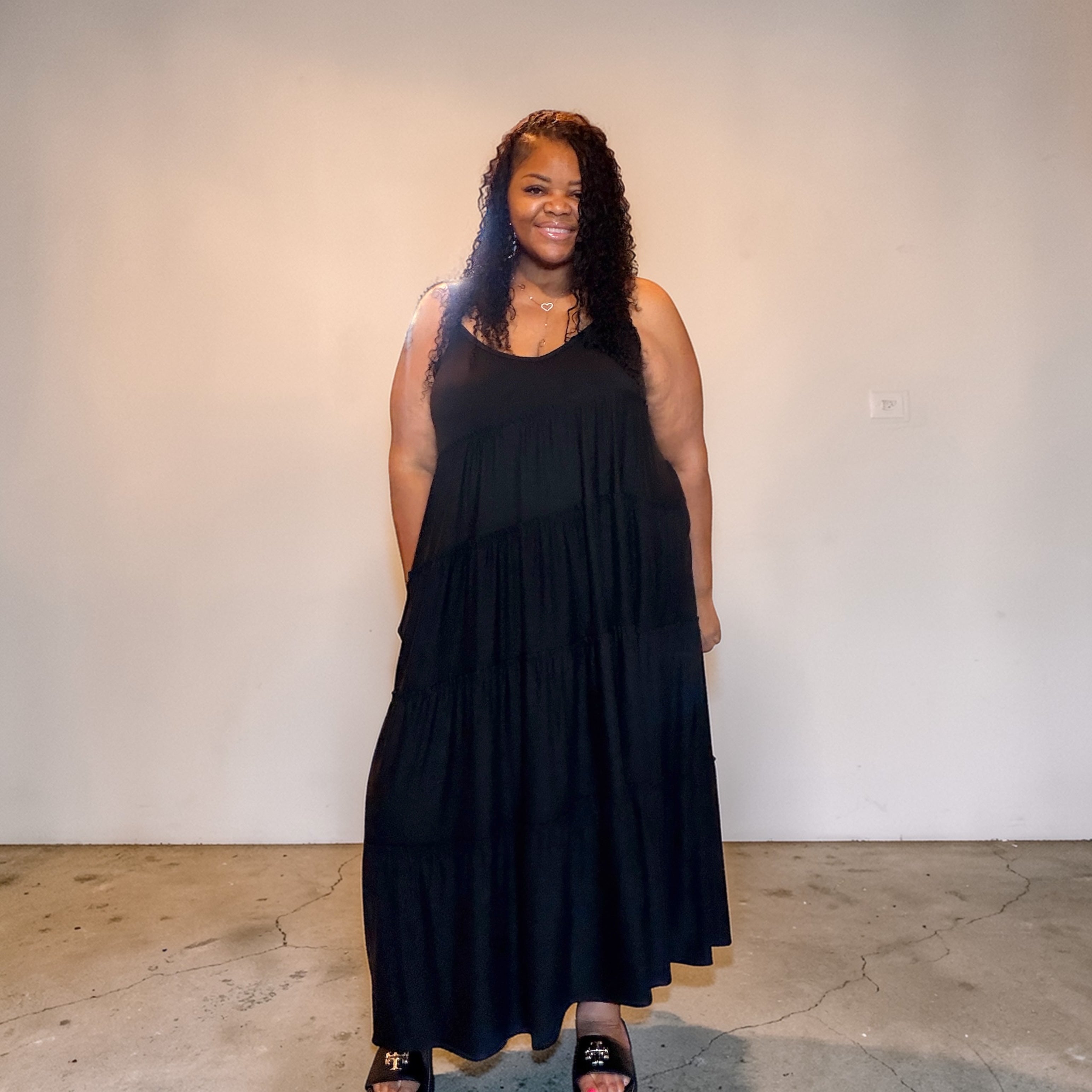 Woman wearing a black dress standing against a plain white wall.